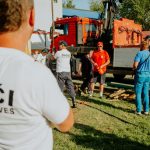 A group of firefighters in a park setting during a public demonstration near a fire truck.